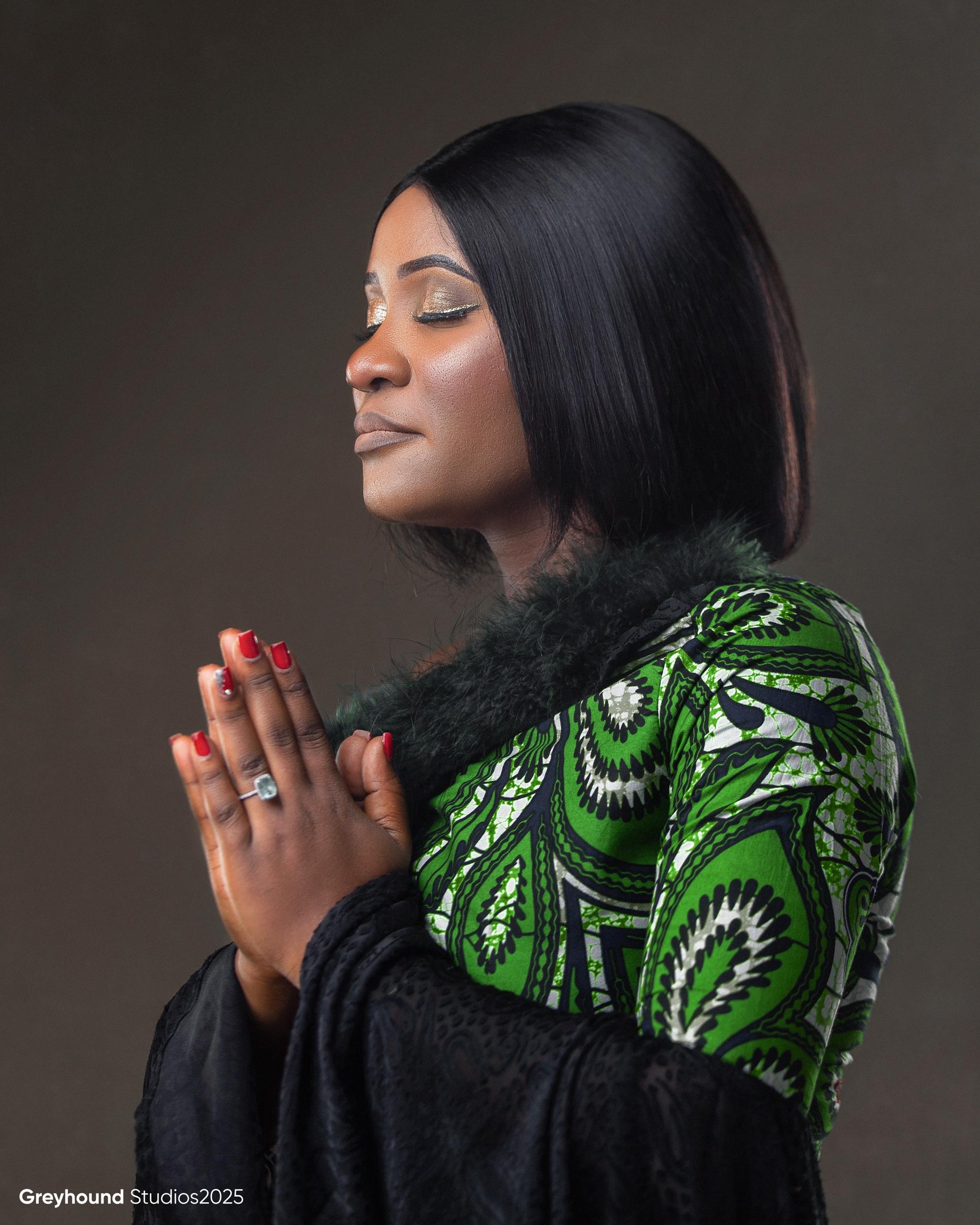 Tendai Makoni in contemplative prayer pose wearing green African print dress with fur trim